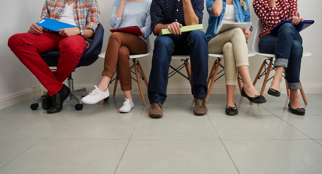 People sitting in a row on a bench, focused on their feet