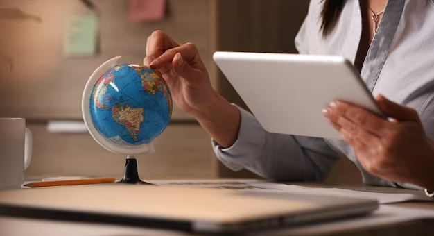 Hand holding a tablet and pointing on a globe with the other hand