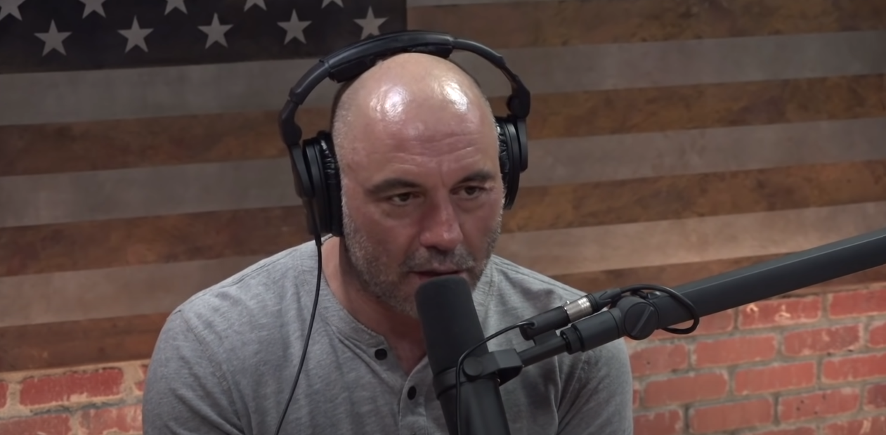 Joe Rogan in gray shirt, wearing headset, speaking into microphone