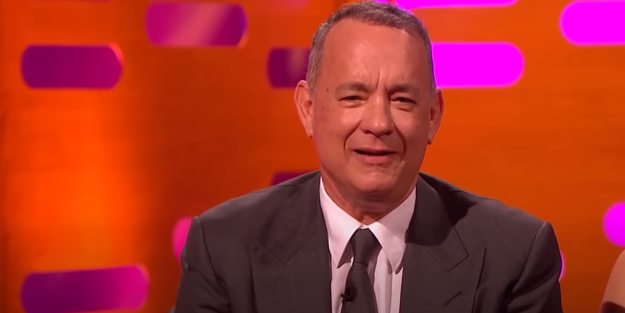 Tom Hanks in a suit against an orange background