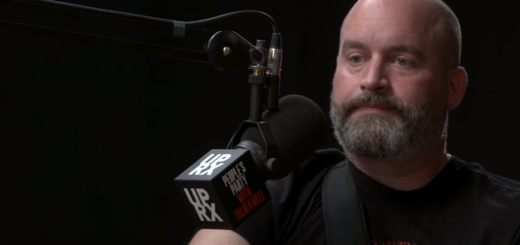 Tom Segura in front of a microphone against a dark background