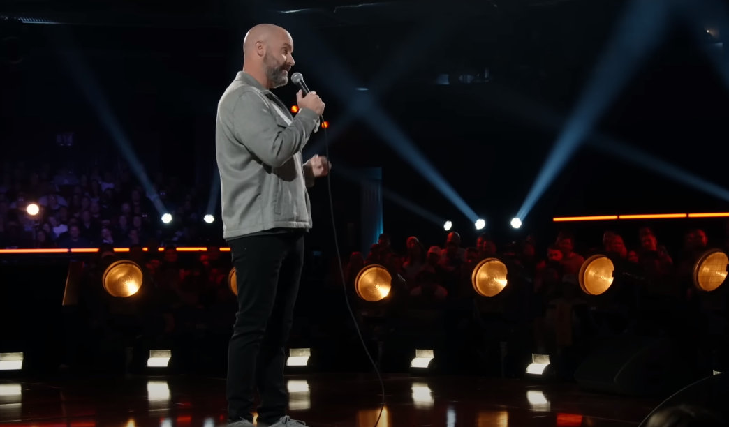 Tom Segura speaking into a microphone on stage