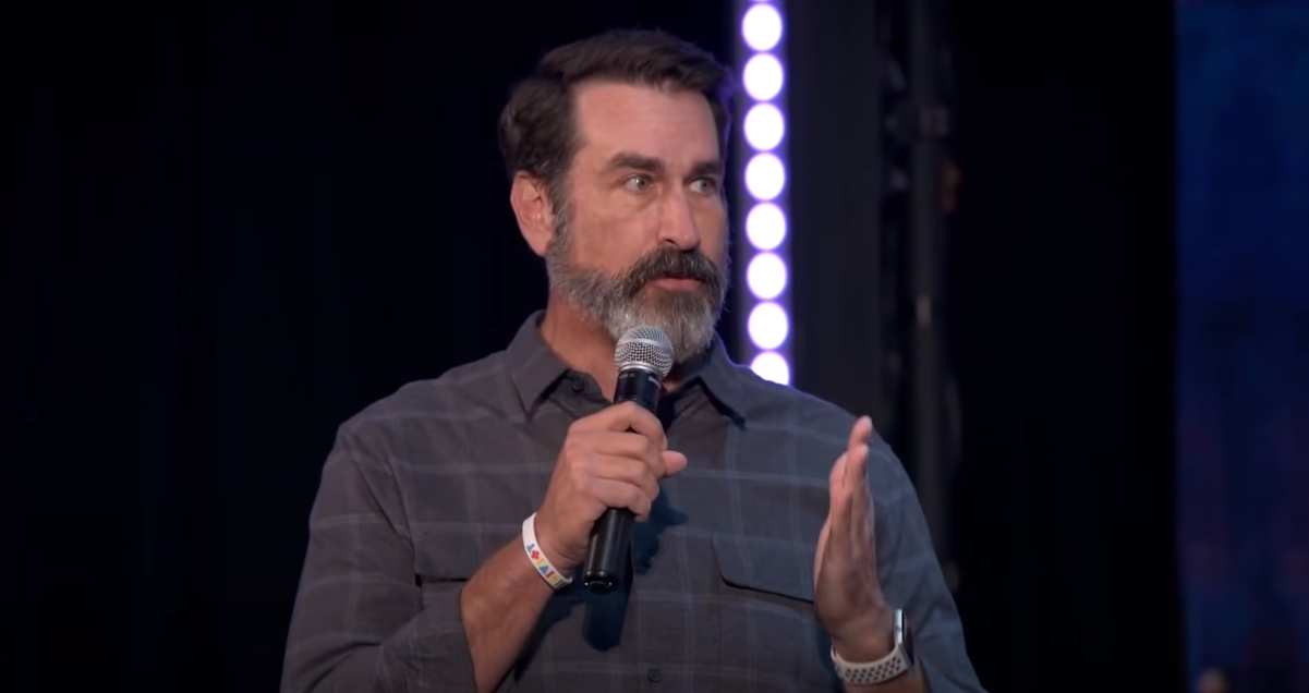 Rob Riggle holding a microphone and speaking