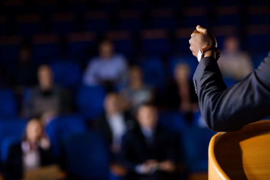 View from behind the camera, showing a man's hand and a crowd of audience