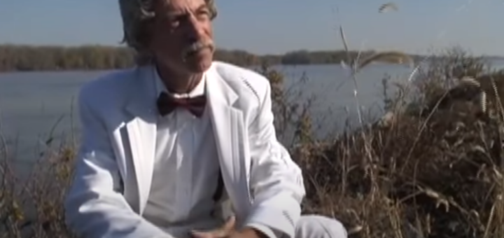 Mark Twain sitting outdoors by the lake amidst grasses