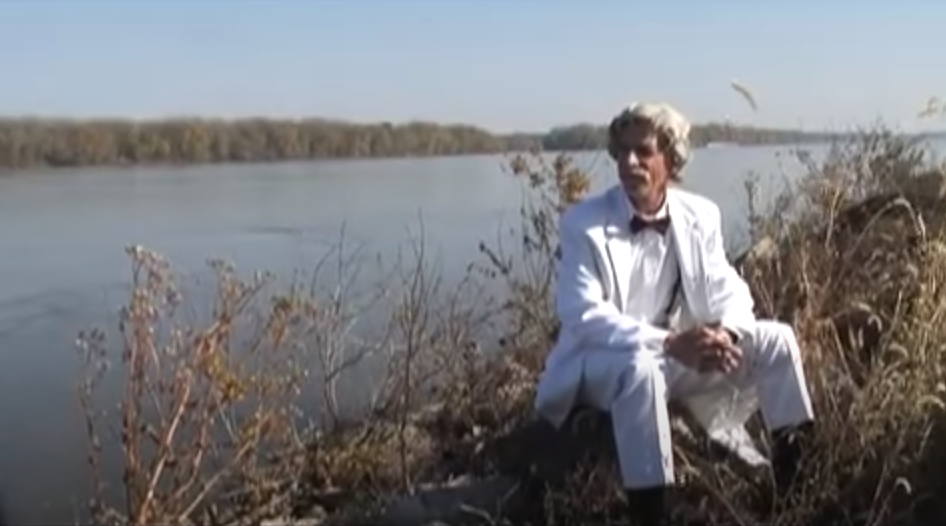 Mark Twain sitting outdoors by the lake amidst grasses