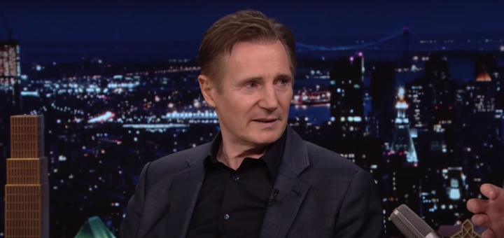 Liam Neeson in a suit against a cityscape night background
