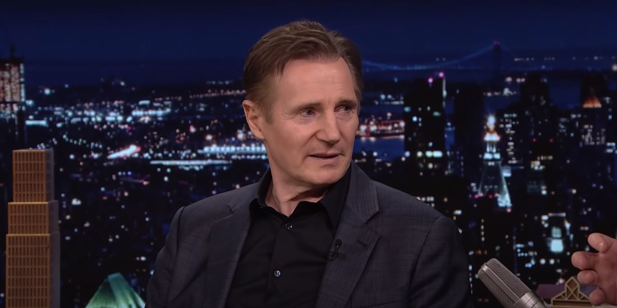 Liam Neeson in a suit against a cityscape night background