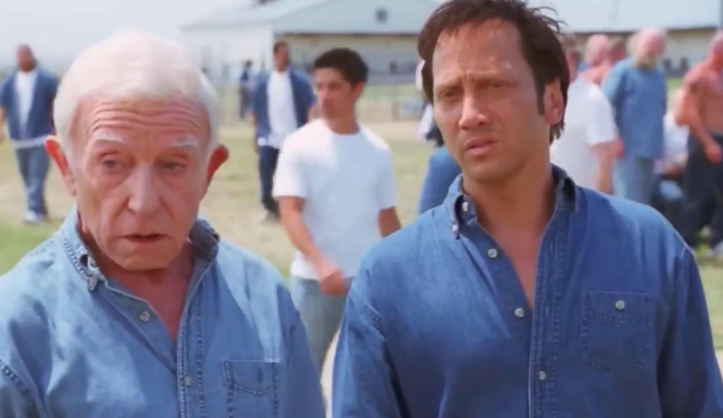Rob Schneider standing near an old man in jeans shirt and looking forward