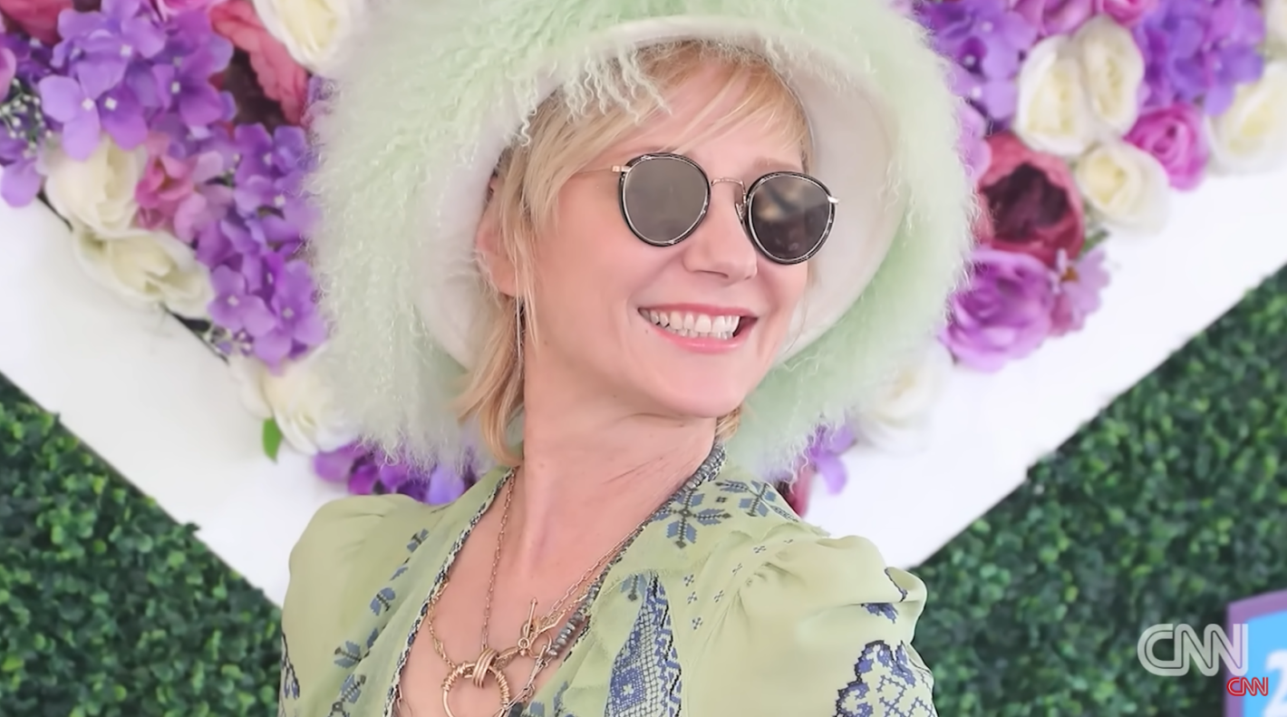 Anne Hache in white fluffy hat, black sunglasses and green blouse with flowers behind her