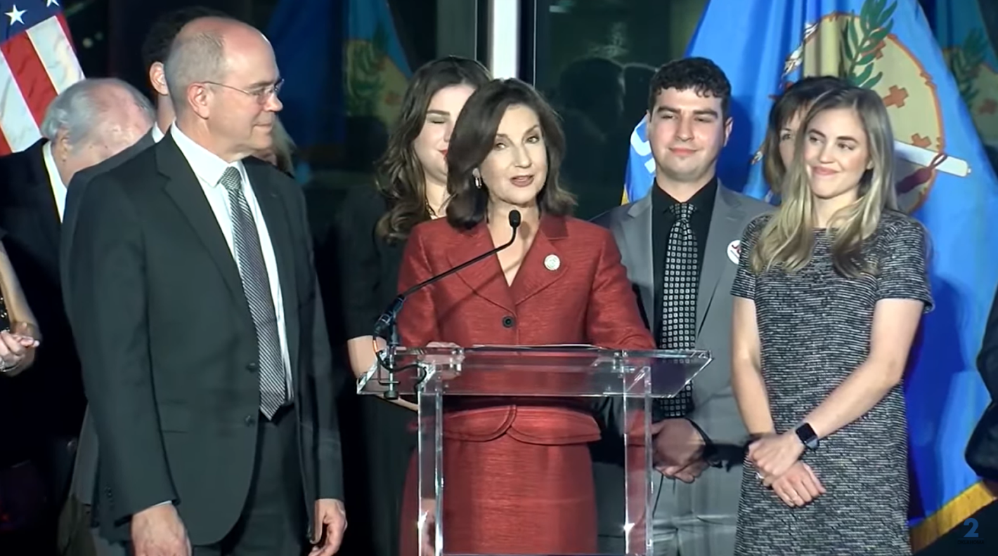 joy hofmeister standing on stage and speaking to microphone among other people