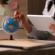Hand holding a tablet and pointing on a globe with the other hand