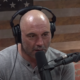 Joe Rogan in gray shirt, wearing headset, speaking into microphone